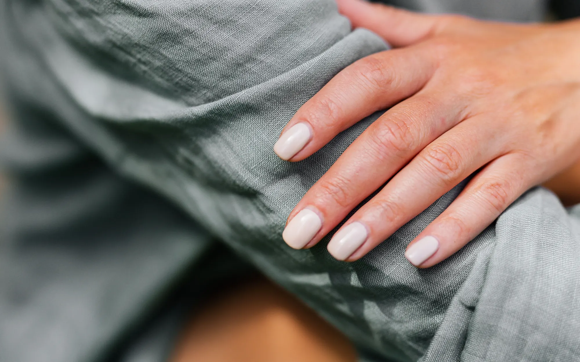 Main aux ongles nude posée sur un tissu gris clair