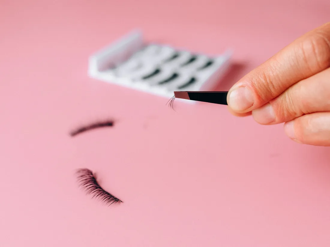 Cils à poser et pince posés sur un fond rose