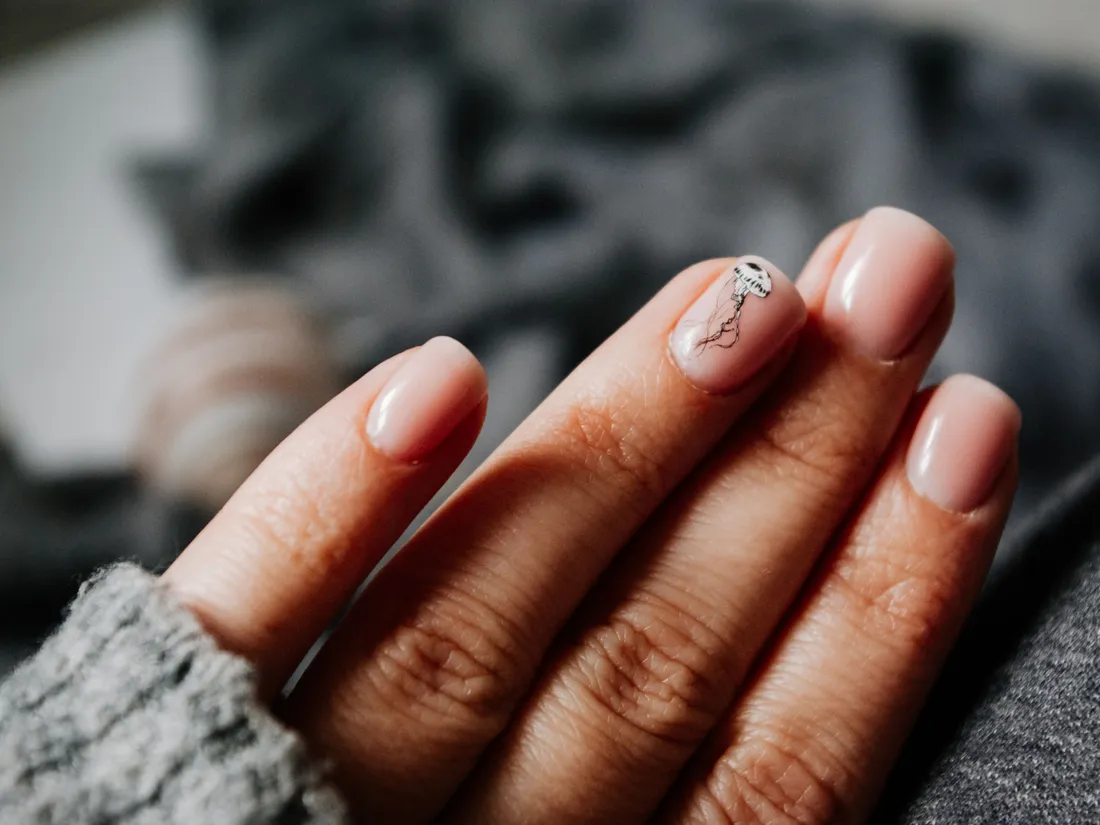 Main aux ongles nude posée sur une maille grise